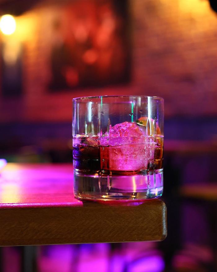 Cóctel sobre hielo con luces de neón de fondo en la barra