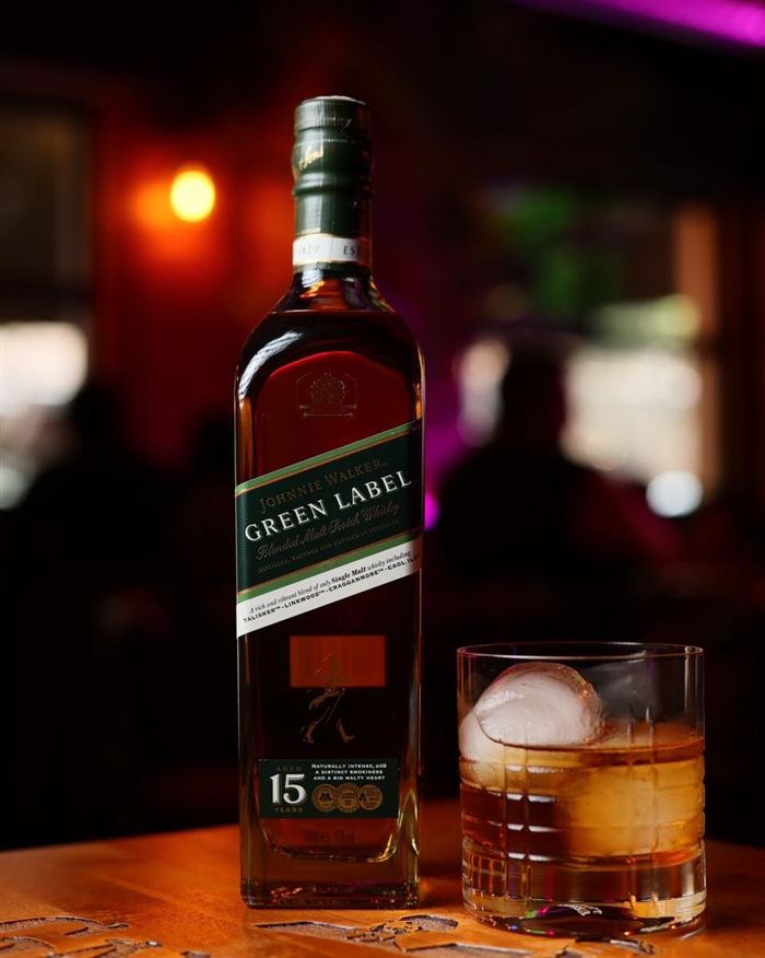 Botella de Johnnie Walker Green Label junto a un cóctel con hielo